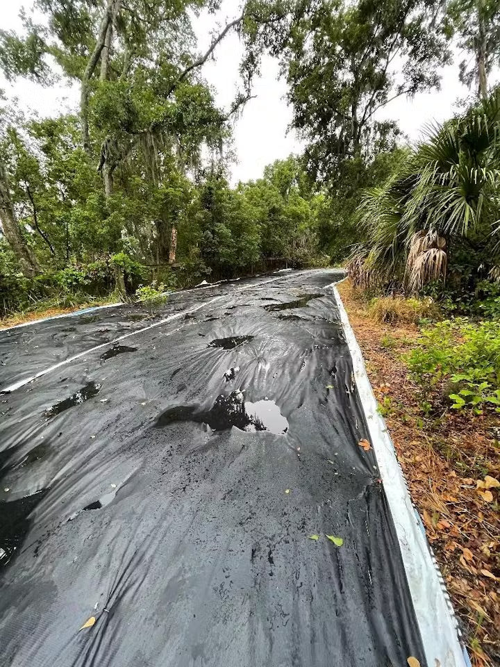 Worker securing an upcycled billboard tarp over a large dumpster container for outdoor storage